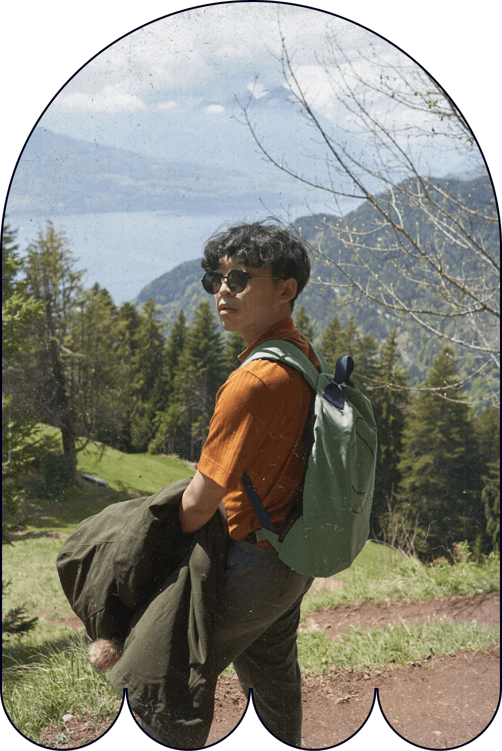 Yanch standing on a path with mountains, trees, and water in the background.
